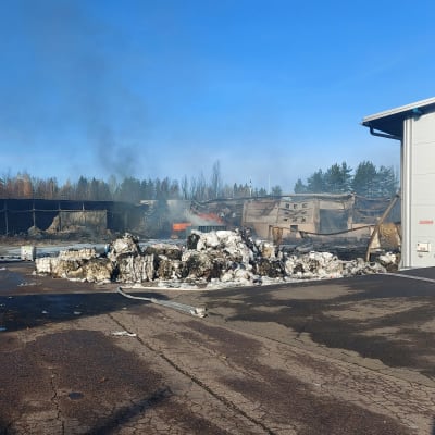 Muovinkierrätyshallin savuavat rauniot teollisuusalueella lokakuun auringossa.