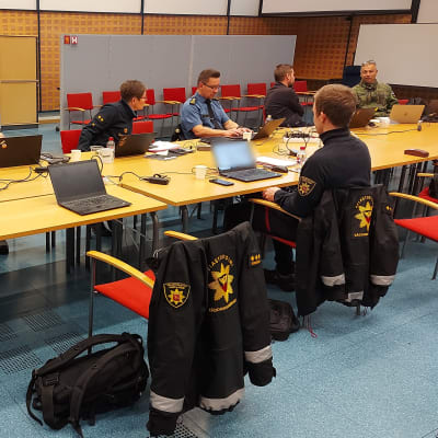 Pelastuslaitoksen ja poliisin työntekijöitä istuu ison pöydän äärelllä.