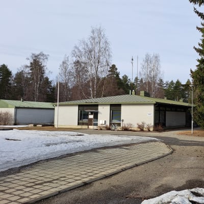 Joensuun hautausmaan kaksi toimistorakennusta kuvattuna selkeänä kevätpäivänä vuonna 2023. Maassa hieman lunta ja kuvan etualalla oikealla hautausmaan toimisto -kylttii.