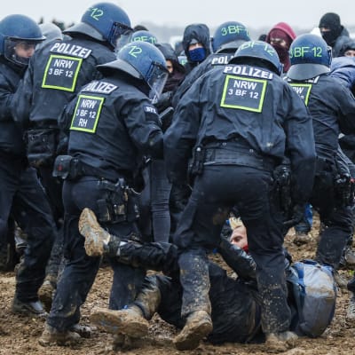 Mellakkavarusteisia poliiseja mutaiseen maahan kaadetun mielenosoittajan ympärillä.