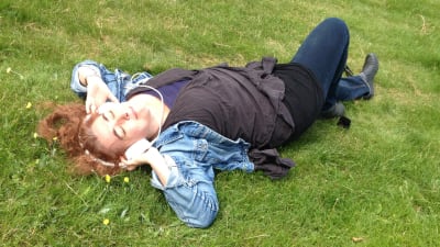 kvinna ligger i gräset med hörlurar