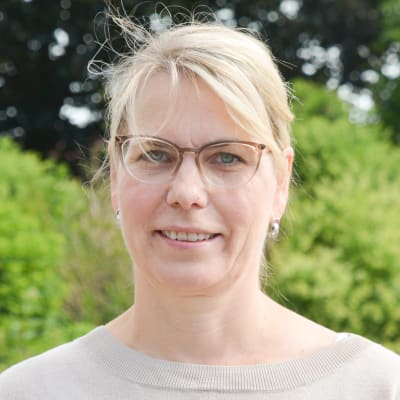 Johanna Tamminen utomhus i en grön miljö i beige tröija. 