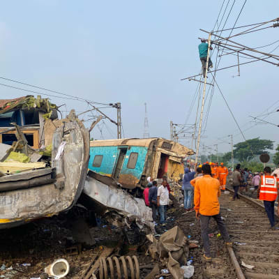 Människor står kring mosade tågvagnar efter en storolycka i den indiska delstaten Orisha.