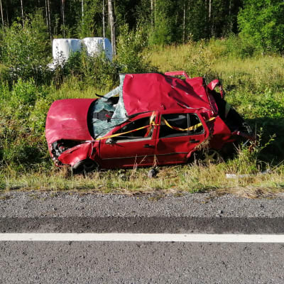 En röd personbil som varit med om en trafikolycka ligger i diket.