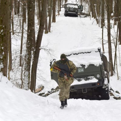 En ukrainsk soldat går förbi ett förstört rysk militärfordon på en snöig skogsväg