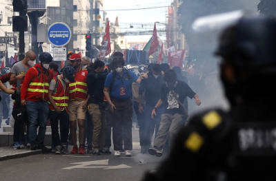 I förgrunden syns en polis som tittar på demonstranter på en gata. Flera av dem har munskydd på sig.