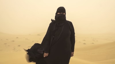 Hissa Hilal står ute i öknen under en sandstorm.
