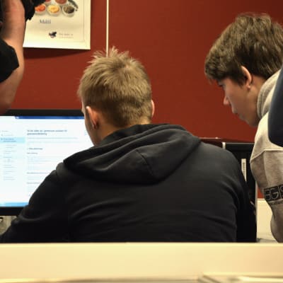 Två ungdomar sitter med ryggen mot kameran vid en dator i en skola