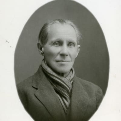 Vanhassa mustavalkoisessa valokuvassa on mies, jolla on kaulaliina ja pukutakki.