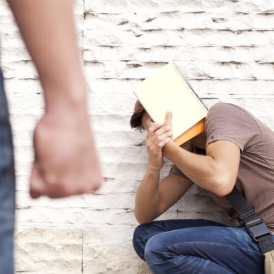 en man sitter tryckt mot en vägg, en annan står med knuten näve och tittar