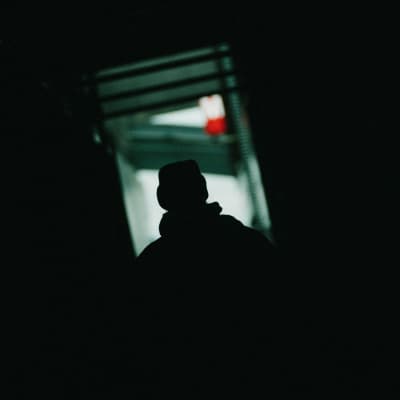 Anonyymi henkilö seisoo pimeässä käytävässä.