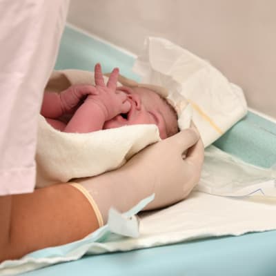 En nyförlöst bebis som en skötare håller om på ett skötbord.