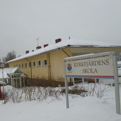 En gul skolbyggnad täckt av snö. I förgrunden syns en skylt där det står Kyrkfjärdens skola.