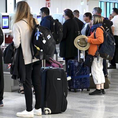Ihmisiä lentokentällä matkalaukkujen kanssa jonottamassa matkalaukkujen jättämiseen.