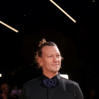 Duudsoneiden Jukka Hildén puolikuvassa mustassa kauluspaidassa mustaa taustaa vasten ponnari päässään.