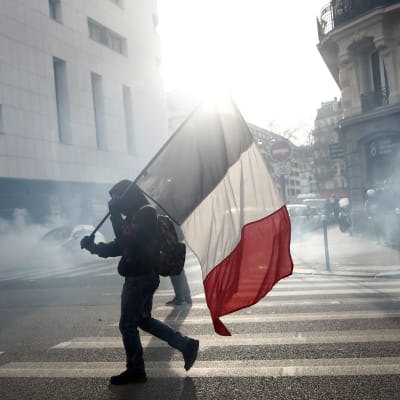 Ranskan lippua kantava mielenosoittaja taustalla savua.