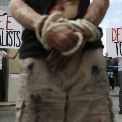 händer förbundnda med skyltar i bakgrunden som uppmanar att avsluta tortyr och mördandet av journalister