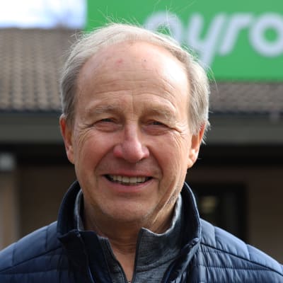 En äldre man tittar in i kameran och ler.