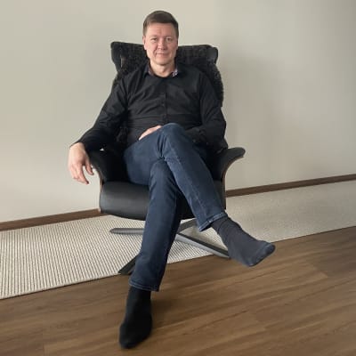 Mies istuu tuolilla ja katsoo kameraan.