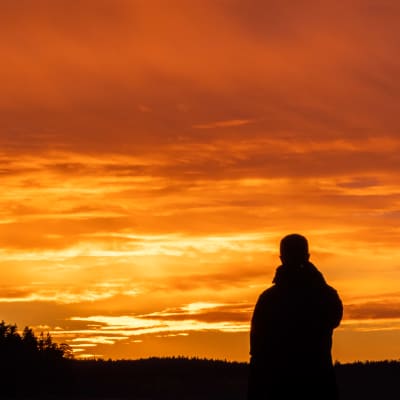 En person tittar mot en solnedgång som färgar hela himlen orange.