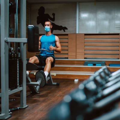 En man i munskydd tränar på gym.