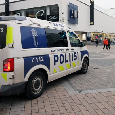 En polisbil i centrum av en stad. I bakgrunden syns ett köpcenter.