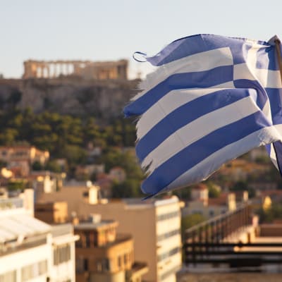En trasig grekisk flagga med Akropolis i bakgrunden.