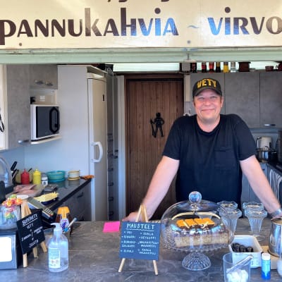 Antti Pyysing omassa vetykahvilassaan Lappeenrannan kauppatorilla. Pyysing nojaa pöytään, hymyilee ja katsoo kameraan.