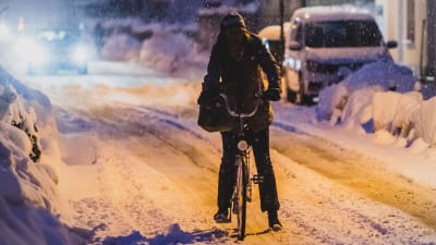 En person cyklar i snöigt väder en kväll.