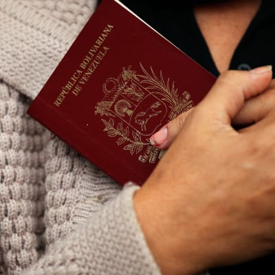 Lähikuvassa kädet pitävät passia kiinni rintaan.