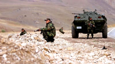 Soldater i kamouflagedräkt står på knä runt ett pansarfordon.