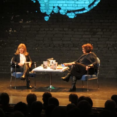Malou von Sievers och Monika Fagerholm samtalar på en scen. Många i publiken tittar på.