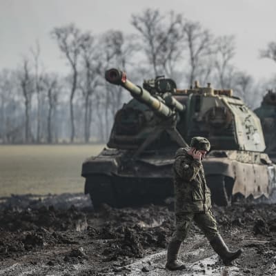 En rysk soldat talar i telefon och vandrar på en lerig väg framför två pansarvagnar.