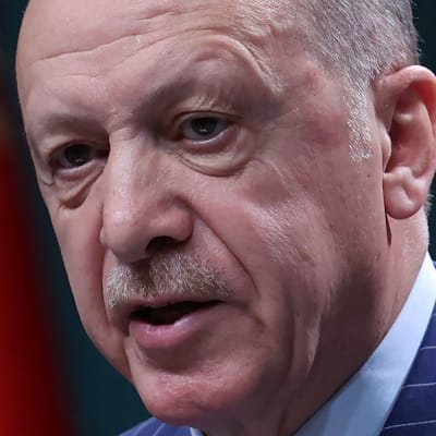 Närbild av Turkiets president Recep Tayip Erdoğan. I bakgrunden turkiska flaggor.