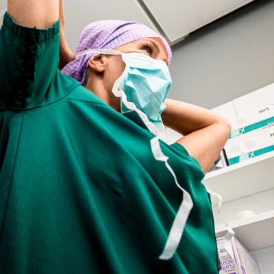 en kvinna i grönblå sjukvårdsdräkt och munskydd i en sjukhusmiljö