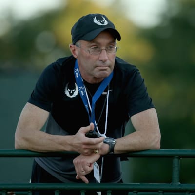 Alberto Salazar står och lutar mot ett räcke med ett tidtagarur i handen.