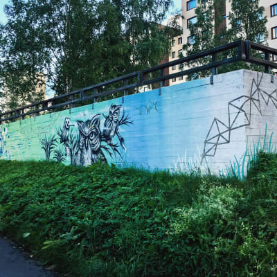 Suojamuuri kadunvarrella, muuriin maalattu sinivihreäsävyinen pöllö