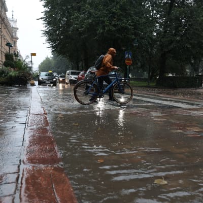 En cyklist leder sin cykel genom en vattenpöl vid ett övergångsställe.