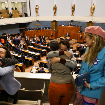 Transhenkilöitä halaamassa  eduskunnan istuntosalin yleisölehterillä.