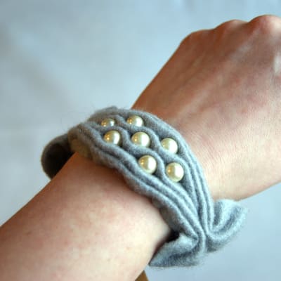 Ett armband av rynkat grått filttyg med pärlbroderi som är knutet runt en handled.