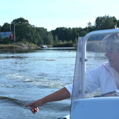 En kvinna i en båt pekar på växter i vattnet.