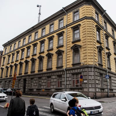 Stenhus i fyra våningar. Fasaden är gul frånsett första våningen som är grå. us i Rödbergen i Helsingfors. Fasaden är gul. Skyddspolisens högkvarter i Helsingfors.