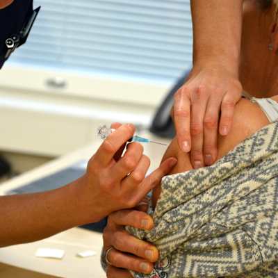 En hälsovårdare vaccinerar en kvinna genom att lägga en spruta i ena armen.