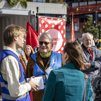 Valkampanj på Sergels torg i Stockholm: två kvinnor talar med två personer i blå partivästar medan en äldre man ser på en bit ifrån.