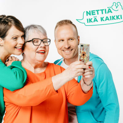 Nettiä ikä kaikki -kampanjan kärkihahmot Anna-Liisa Tilus ja Mikko Kekäläinen katsovat älypuhelimen ruutua yhdessä eläkeikäisen naisen kanssa. Kuvassa on teksti Nettiä ikä kaikki.