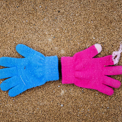 En blå och en rosa handske på marken.