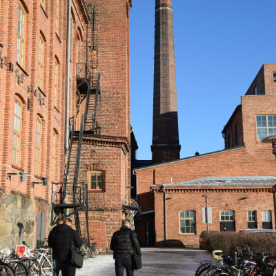 Rödtegelhus vid Vasa universitet. Tre män promenerar över cykelparkering.