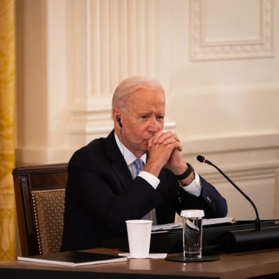 Joe Biden sitter vid ett bord med händerna framför ansiktet och en orolig min.