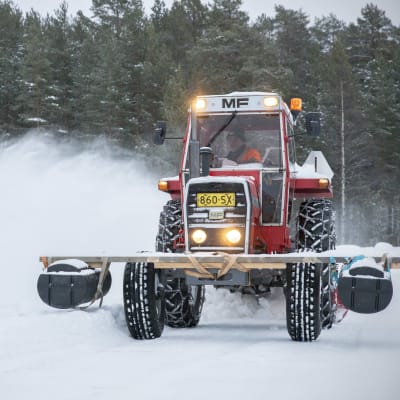 Kellukeponttooneilla varustettu traktori linkoaa lunta pois jäätieltä.