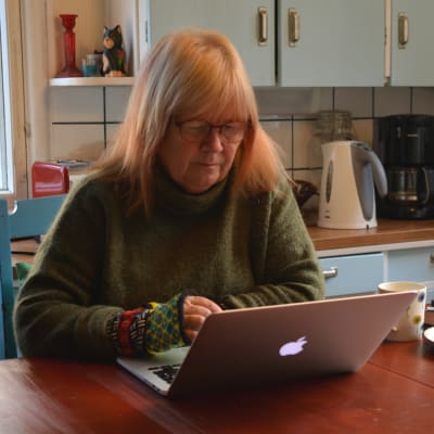 Jaana Kapari-Jatta sitter vid köksbordet, framför sin dator och skriver. 